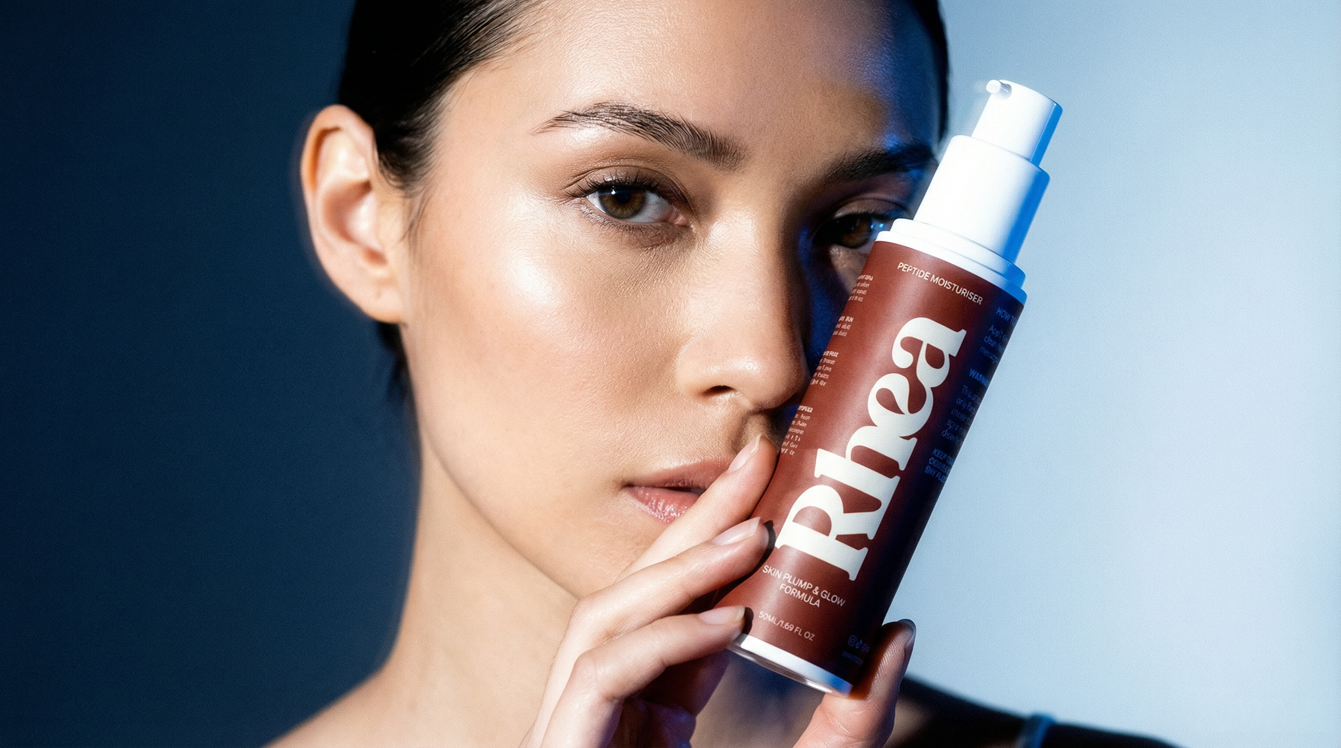 Model holding Rhea peptide moisturiser against a deep blue gradient background.